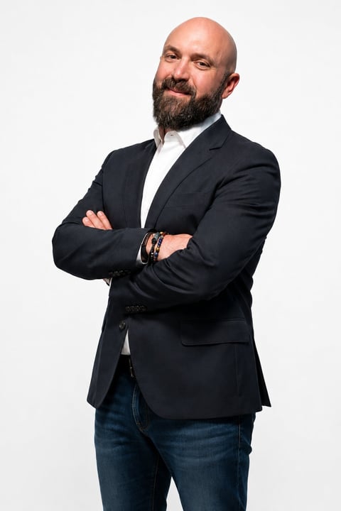 Professional headshot of a bearded man in a dark blazer and white shirt with arms crossed against a white background